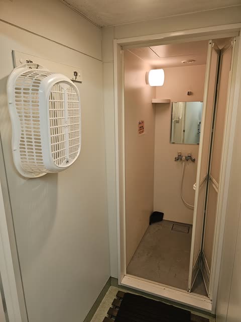 A white plastic laundry basket hangs on a wall next to an open doorway leading into a compact shower stall.