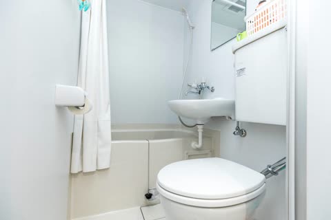 A white bathroom contains a toilet, a sink mounted above the toilet tank, and a bathtub next to a shower curtain.