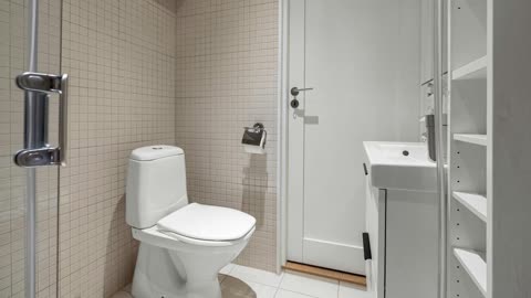 A small bathroom contains a white toilet and sink next to a glass shower door against a beige-tiled wall.