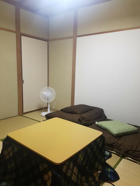 A kotatsu table and futon bedding sit on a tatami mat floor in a room with sliding panel walls.