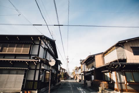 A narrow street runs between traditional Japanese-style buildings, with numerous power lines crisscrossing the sky above.