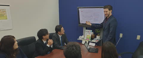 A man in a suit presents a graph on a screen to several people seated at a conference table.