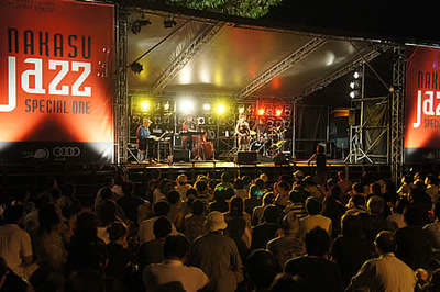 Band performing jazz music on an outdoor stage at night before a large audience.