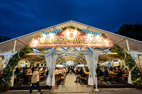 Night view of people seated at tables inside a large illuminated Oktoberfest tent.