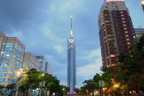 Illuminated Nagoya TV Tower at night, surrounded by buildings and trees.