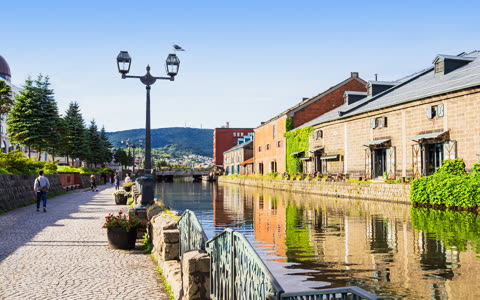 People walking along canal-side path near brick buildings.