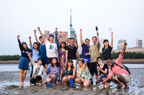 Group of people posing on a beach with tools, arms raised.
