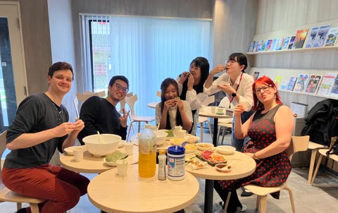 Six people eat at a table in a break room.