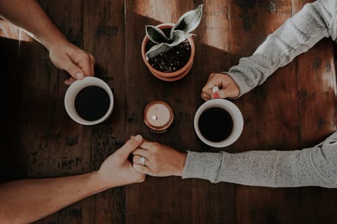 Two people hold hands across a wooden table with coffee cups.