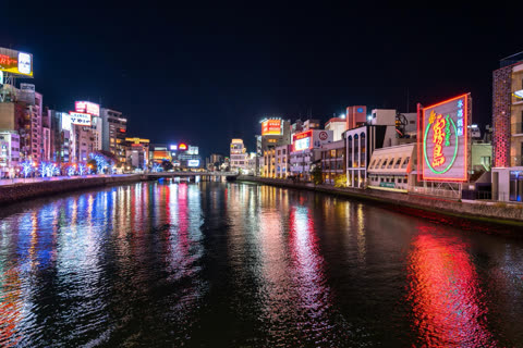 Night view of neon-lit buildings reflected in a calm river.