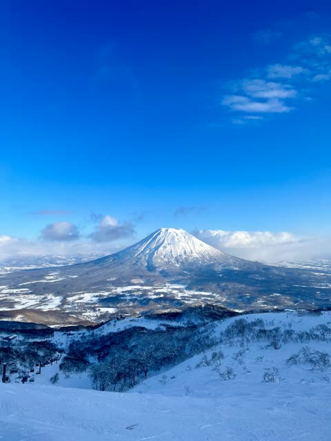 Snow-covered mountain viewed from a snowy hillside under a clear blue sky.
